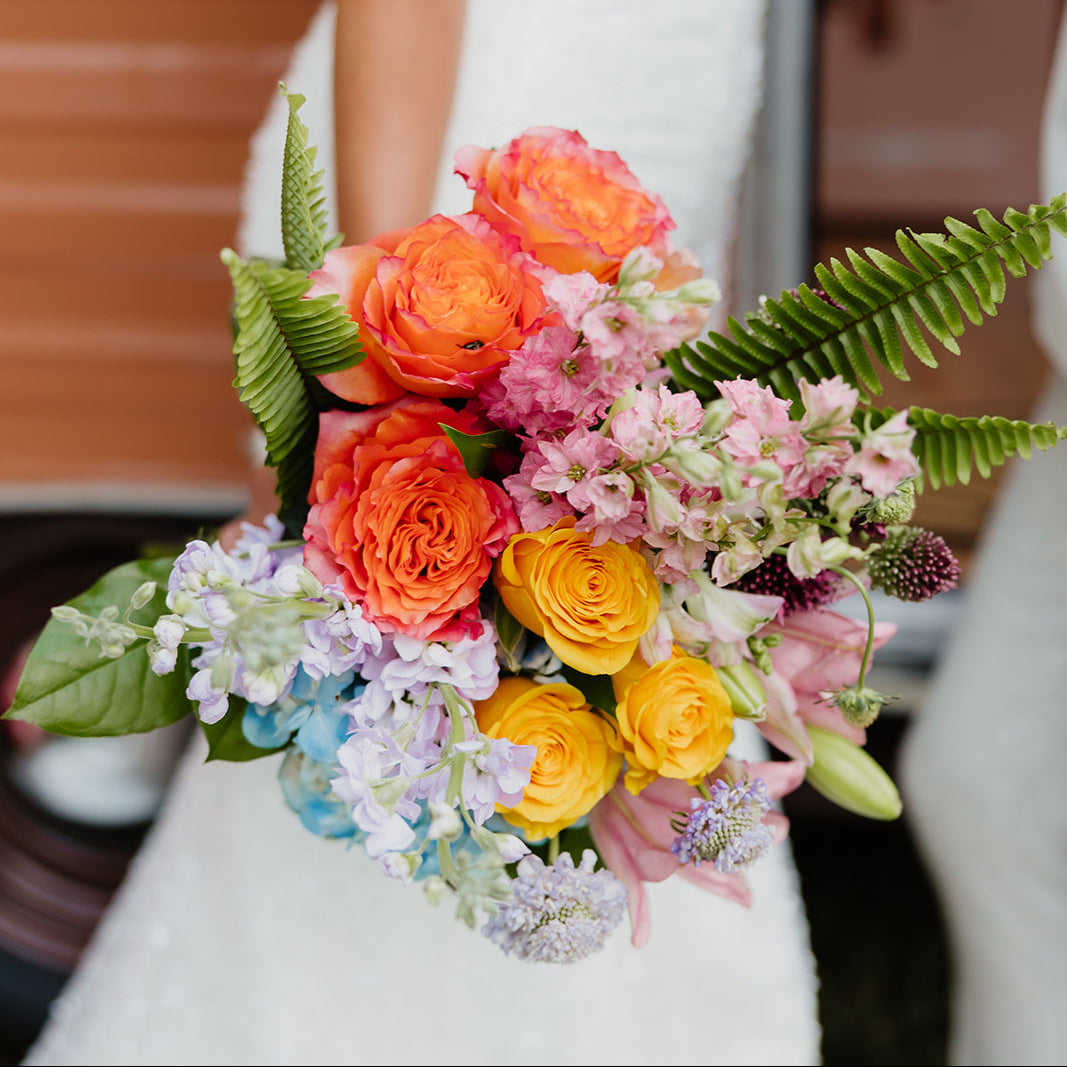Colorful bouquet held by a bride in a white dress with a blurred background